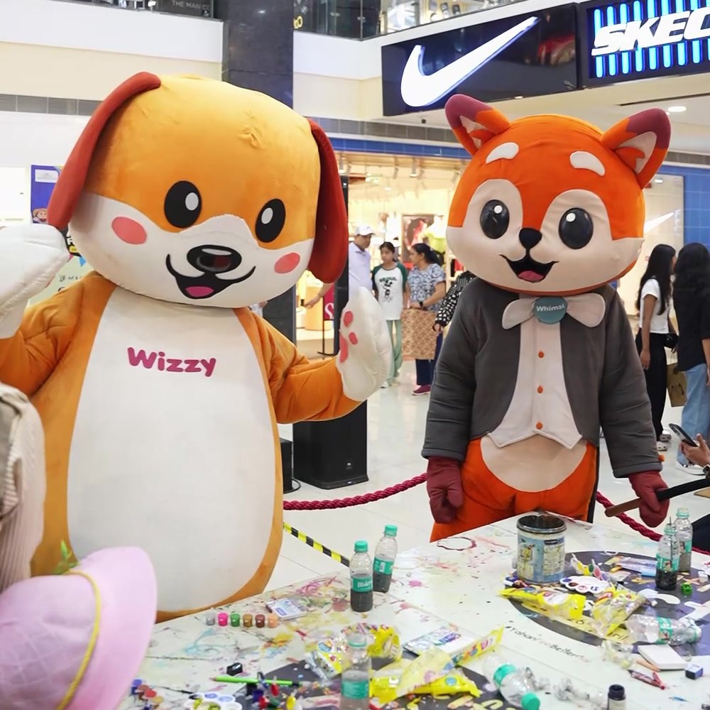 Both mascots behind a craft table covered in paint and materials