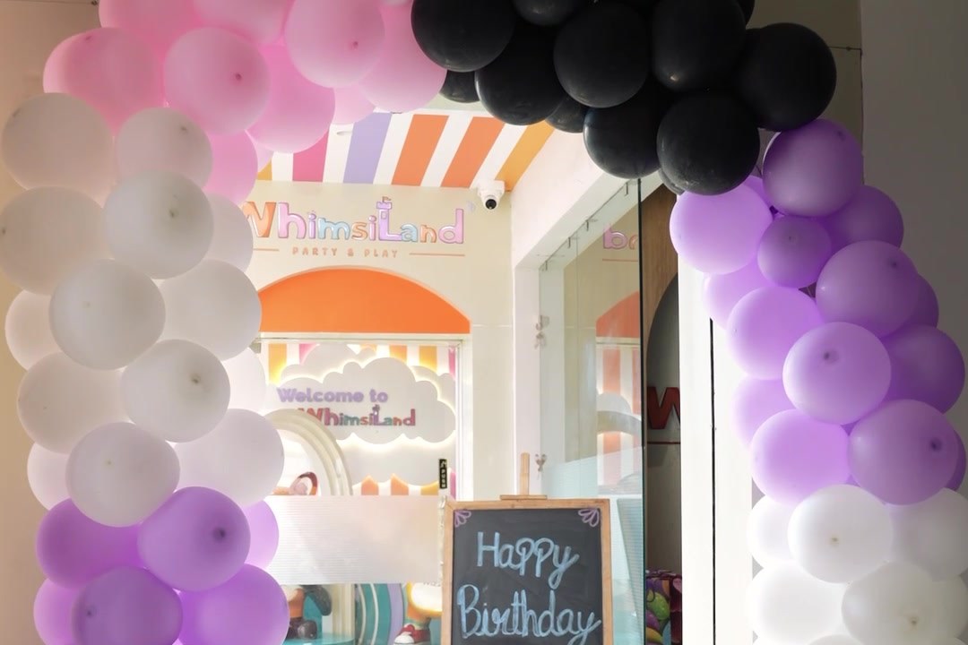 A balloon arch framing the WhimsiLand entrance with a Happy Birthday chalkboard