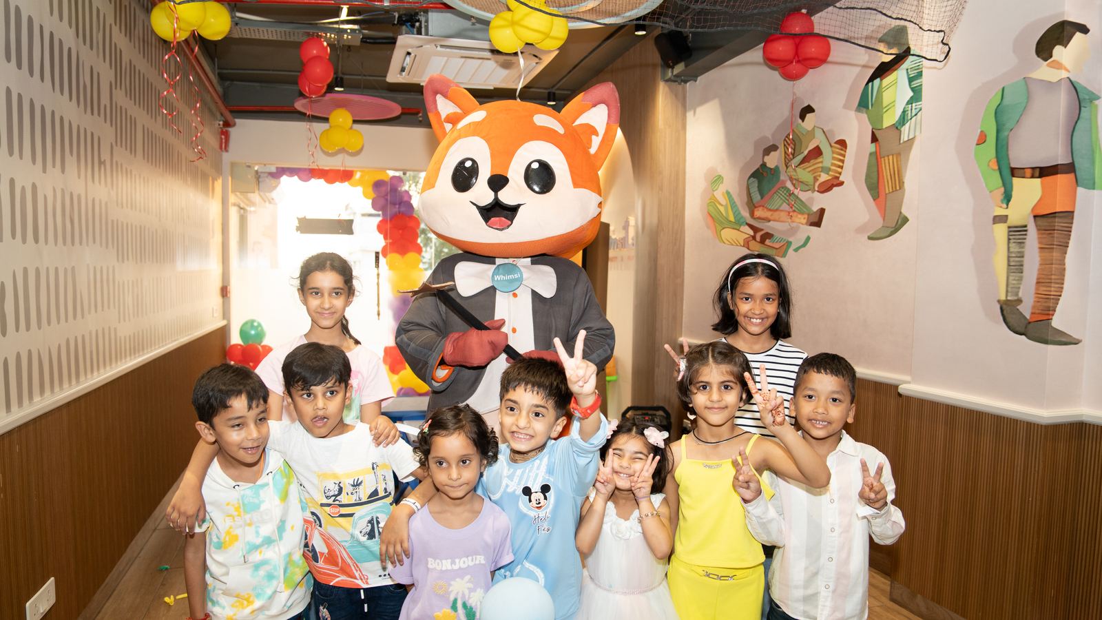 Whimsi the mascot surrounded by a birthday party group, all posing for the camera