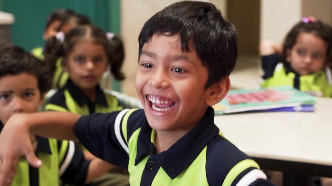 A boy in school uniform laughing at a café table with his classmates around him